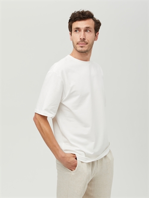 Белая мужская футболка COSHENE, вид спереди, модель в светлых брюках